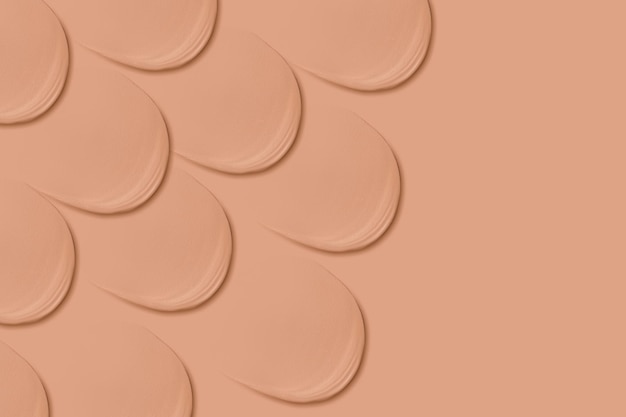 Many identical strokes of foundation on a beige background Dark color