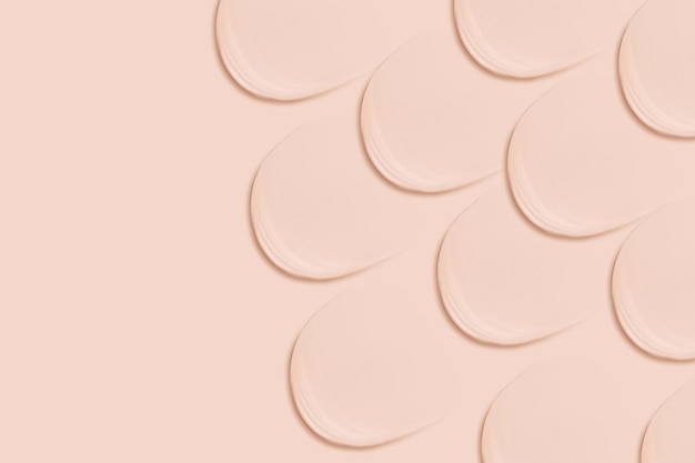 Many identical strokes of foundation on a beige background Light color