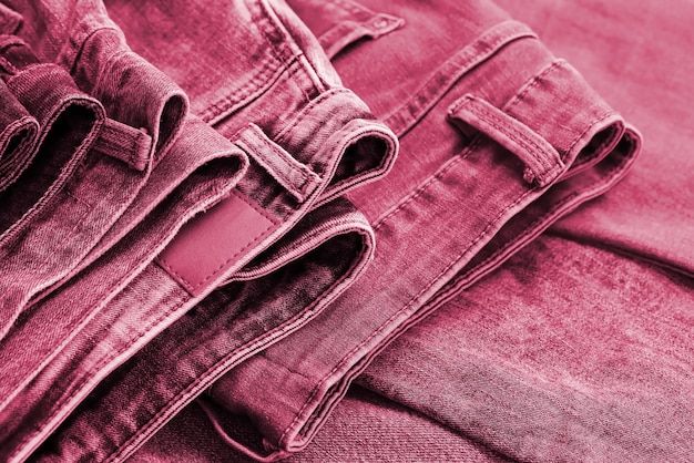 Many jeans in stack in wardrobe room Row of pants denim jeans in closet Concept of buy sell shopping and fashionable clothes Image toned in Viva Magenta color of the 2023 year