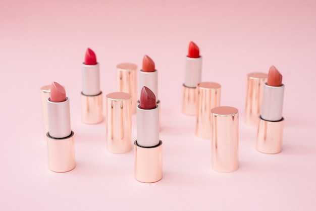 Many luxury gold lipsticks in different shades of pink stand on a pink pastel background