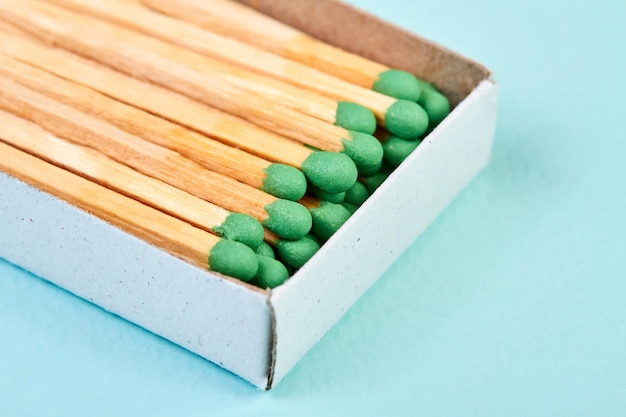 Many matches with green heads in a matchbox on a blue background with copy space