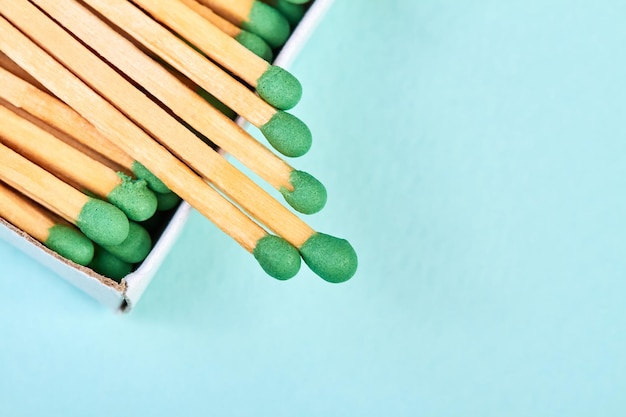 Many matches with green heads in a matchbox on a blue background with copy space