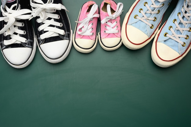 Many multi-colored well-worn textile sneakers of different sizes on a green background, top view, concept family, copy space