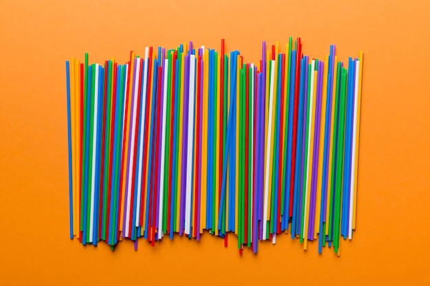 Many multicolored plastic tubes for cocktail on Colored background top view