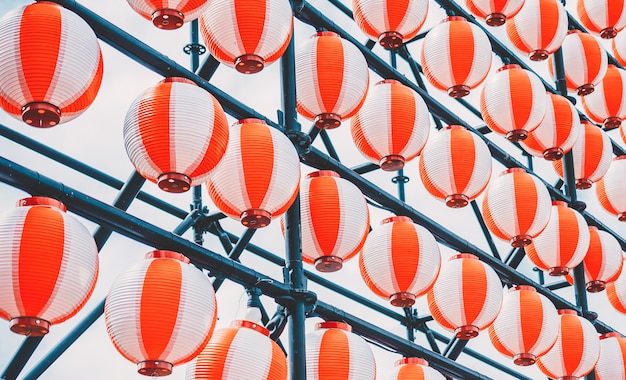 Many paper red-white oriental paper lanterns hanging in a row on blue sky