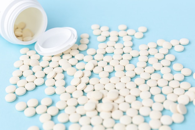 Many pills spilled out of a white plastic can against a blue background.