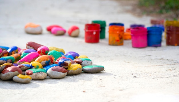 Many small pebbles covered with multicolored paint lie on surface