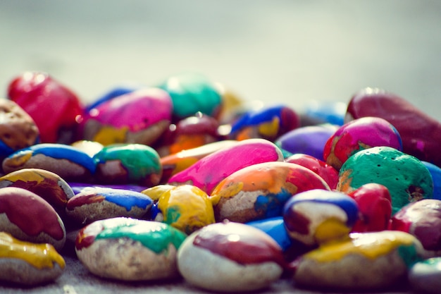 Many small pebbles covered with multicolored paint lie on surface