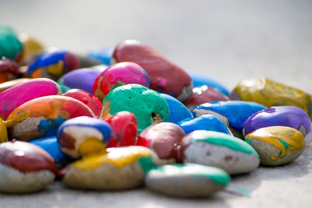 Many small pebbles covered with multicolored paint lie on surface