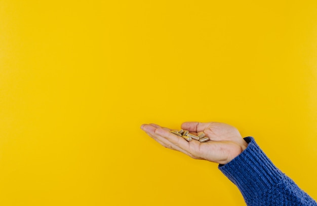 Many tablets pills in a man's hand on a bright yellow background