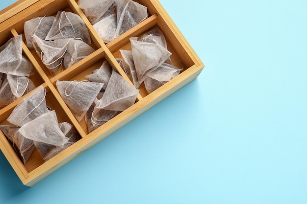 Many tea bags in wooden box on light blue background flat lay Space for text