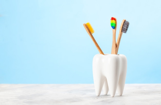 Many toothbrushes in a glass in the form of a tooth. Blue background. The concept of how to choose the right toothbrush.