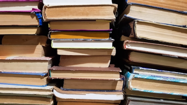 Photo many used old books in the school library. chaotic layout of stacks of literature, selective focus. a pile of books ends with stacked background. books in a library - backdrop.