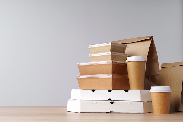 Many various take-out food containers, pizza box, coffee cups and paper bags on light grey background. Food delivery