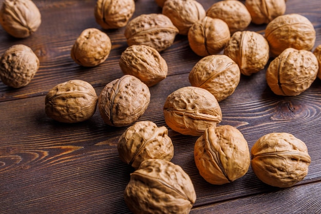 Many walnuts with shells randomly scattered on brown wooden surface