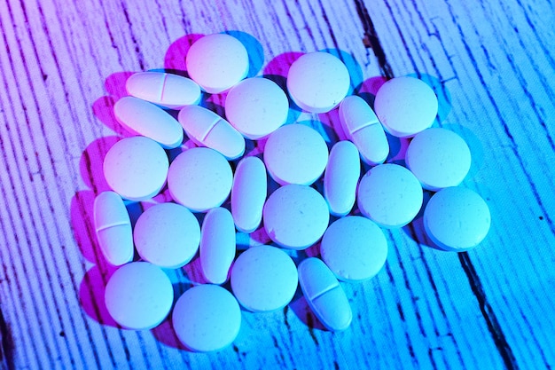 Many white medical pills in row and tablets spilling out white surface Macro top view with copy space