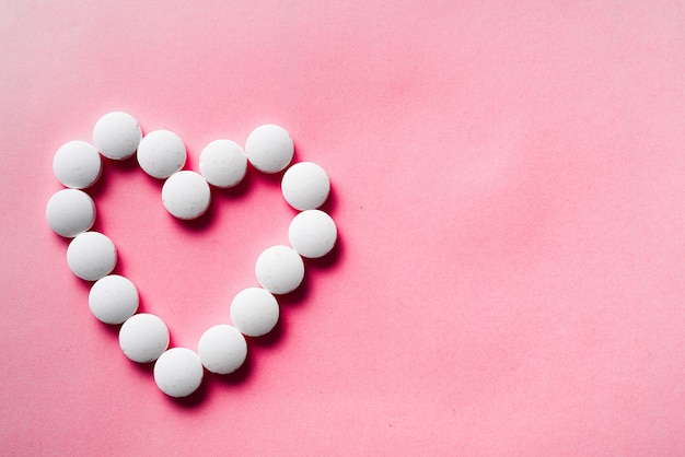 many white pills from heart on a pink background. accept gifts concept. Cardiology or love concept