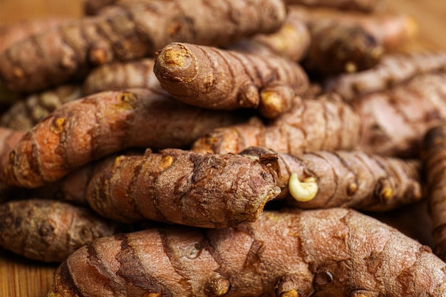 Many whole turmeric roots on wooden table closeup