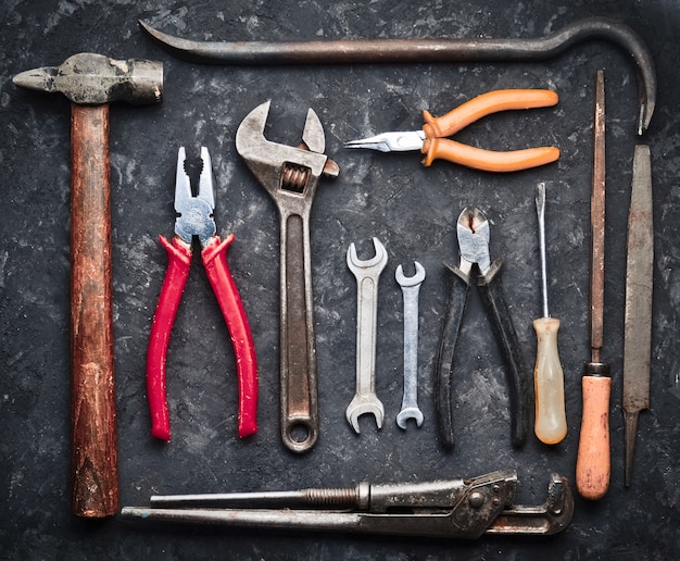 Many working tools on a black concrete table. Nippers, file, pliers, scrap, hammer, wrench, screwdriver. Top view. Flat lay.