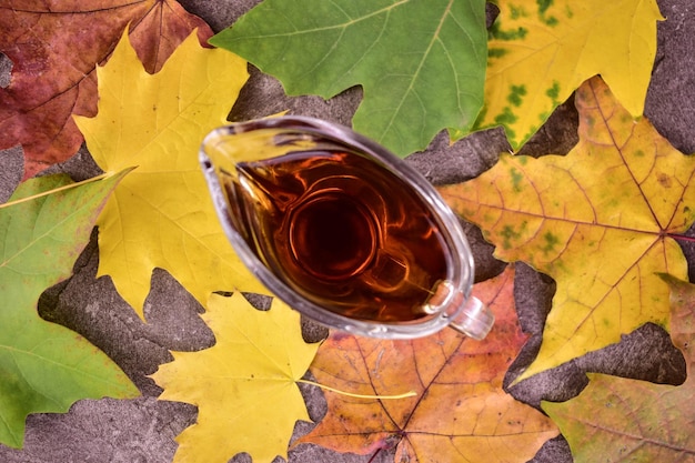 Maple syrup in a glass decanter against a background of autumn maple leaves Flat lei