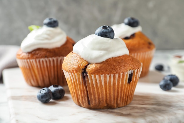 Marble board with tasty muffins cream and blueberries on table