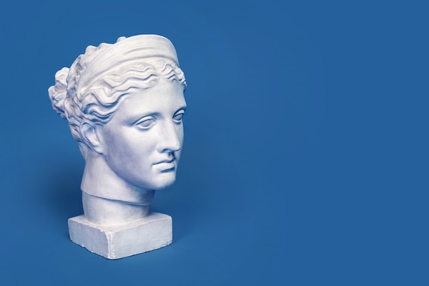 Marble head of young woman, ancient Greek goddess bust isolated on blue background. Gypsum copy of a statue Diana head