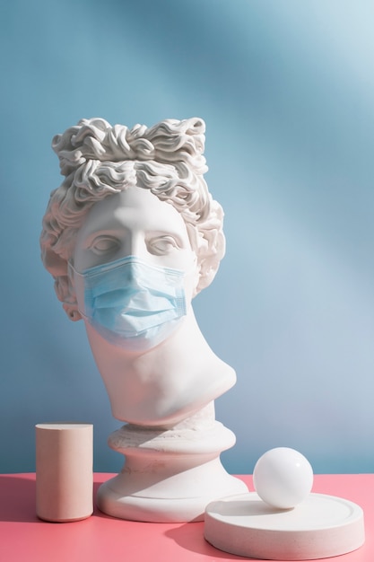 Marble sculpture of historical figure with medical mask and ball on a platform