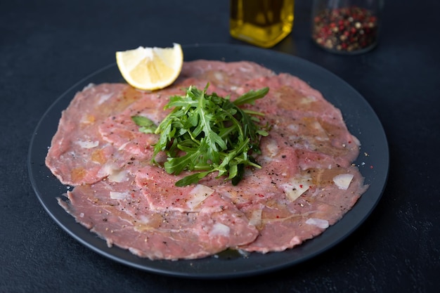 Marbled beef carpaccio with arugula parmesan cheese olive oil and lemon A traditional classic appetizer made from thinly sliced raw meat Closeup selective focus black background