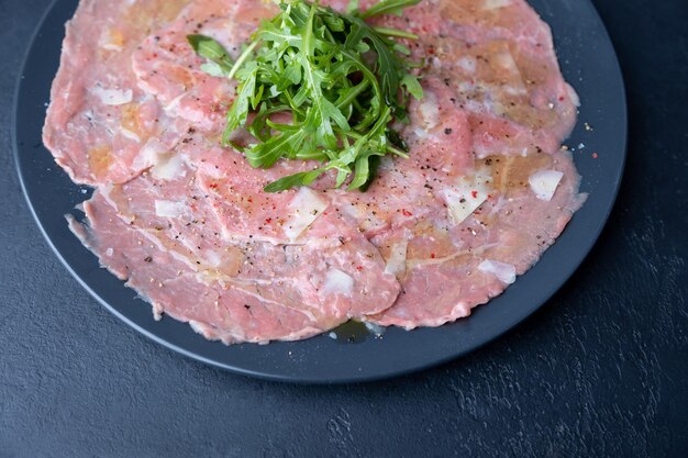 Marbled beef carpaccio with arugula parmesan cheese olive oil and lemon A traditional classic appetizer made from thinly sliced raw meat Closeup selective focus top view black background