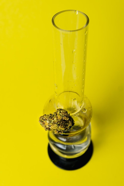 Marijuana bud and bong on yellow background close up