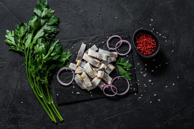 Marinated herring fillet with pepper, herbs and red onion. Black background. Top view.  Space for text