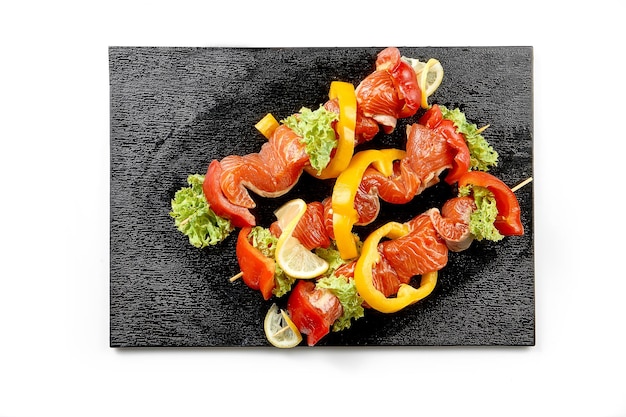 Marinated salmon shashlik with vegetables on a black board on a white background Closeup Selective focus