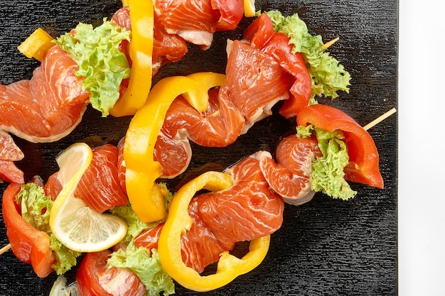 Marinated salmon shashlik with vegetables on a black board on a white background Closeup Selective focus