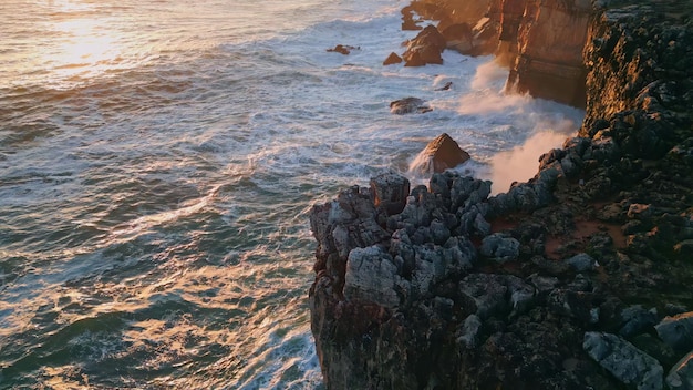 Marine sunset rocky coast washing by stormy ocean powerful sea waves on cliffs