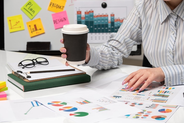 Marketing business lady in striped shirt in office with computer holding coffee cup with glasses