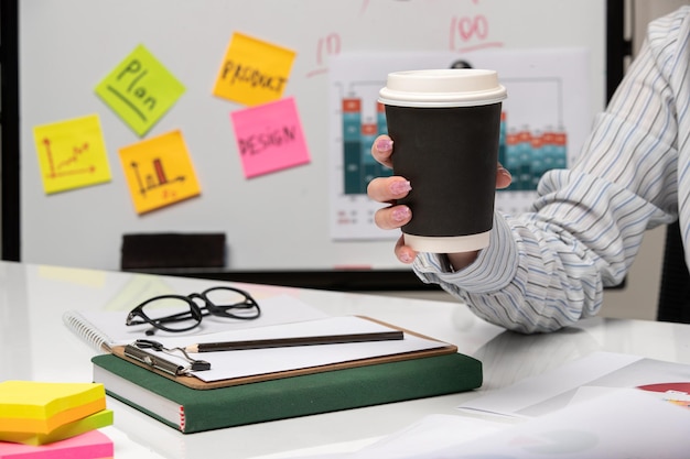 Marketing business lady in striped shirt in office with computer holding paper coffee cup