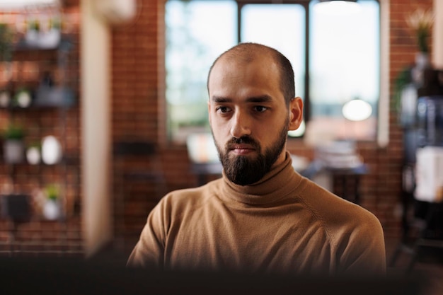 Marketing office employee brainstorming management ideas. Young businessman sitting in office with crossed arms, looking at computer monitor while reviewing financial statistics.