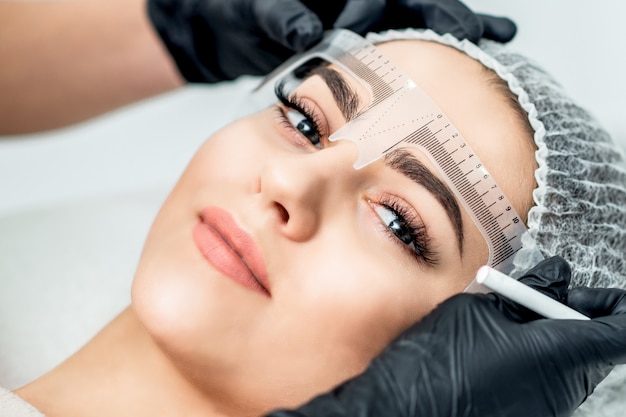 Markup with ruler on eyebrows of yong woman during permanent make up.