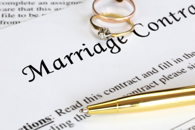 Marriage contract with two golden wedding rings and gold pen prenuptial agreement macro close up sign with signanturedocumentagreement concept