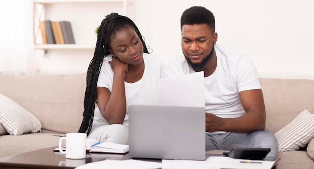 Married afro couple managing family budget at home together, reading mortgage or insurance documents, panorama with free space