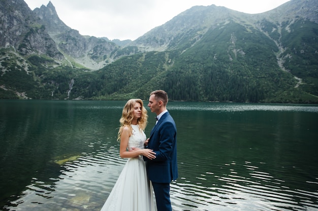 Married couple (bride and groom) getting married in the mountains. hugging in the middle of a lake with a mountain in the background