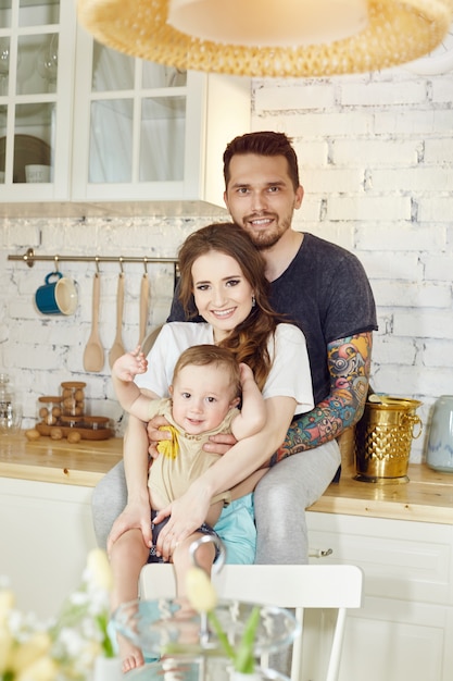 Married couple and their little baby baby in her arms. Young family at home in the morning on a day off. Joyful and happy faces hugging and having fun