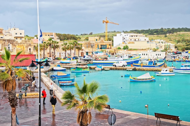 Marsaxlokk, Malta - April 5, 2014: People and Luzzu colorful boats at Marsaxlokk Harbor, Malta island