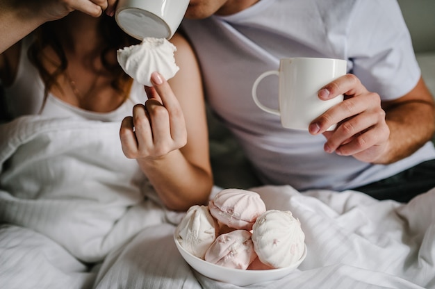 Marshmallow in hand in the background man and a woman drink coffee in bed