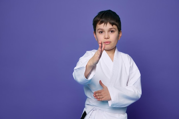 Martial arts attack School age boy aikido fighter in white kimono isolated over purple background with copy space for advertising text