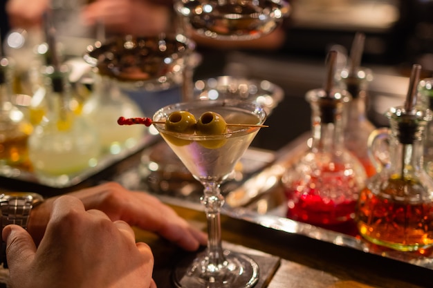 Martini with green olives on a table in bar.