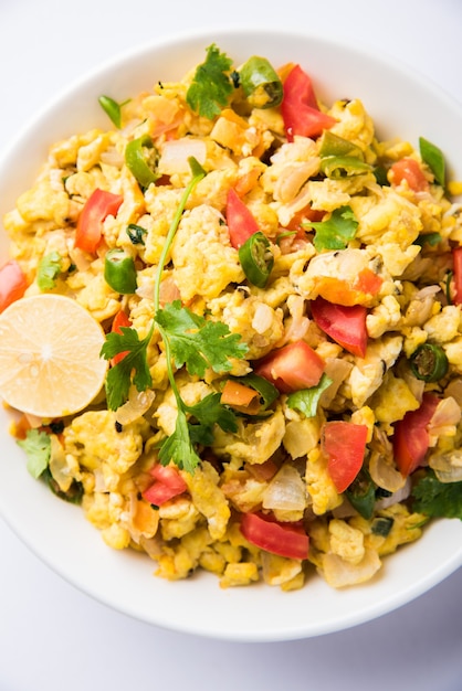 Masala Anda Bhurji or Spicy Indian scrambled eggs, Popular street food in Mumbai. Served in white crockery, isolated over moody background. selective focus