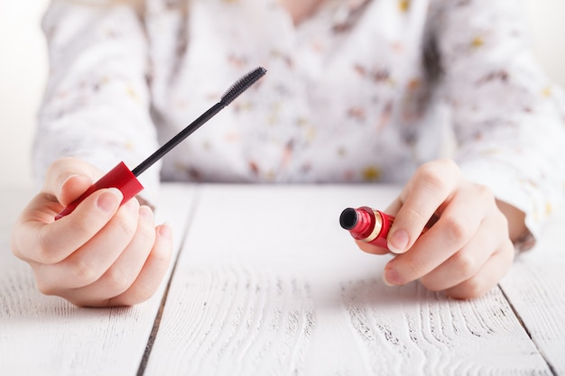 Mascara in female hands on white table