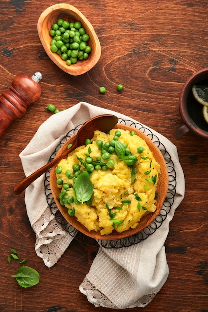 Mashed potato with butter, green peas, onions, basil on a rustic wooden background. Top view with close up.