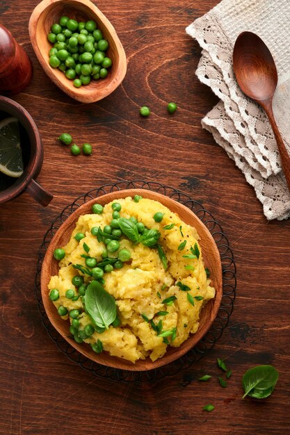 Mashed potato with butter, green peas, onions, basil on a rustic wooden background. Top view with close up.